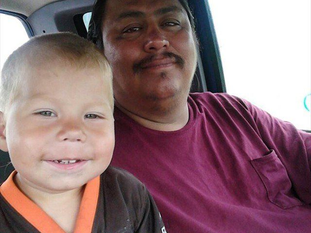 Two people sitting in a car, smiling at the camera, one in a maroon shirt and one in a brown top with orange trim