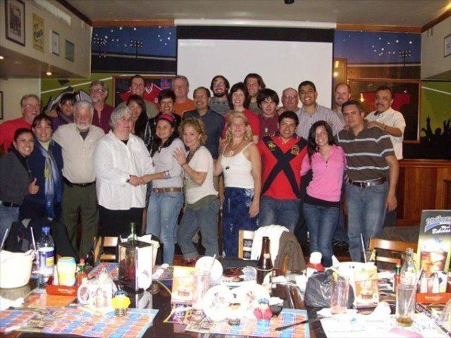 Group of people posing together in a restaurant, gathered around a table with food and drinks.