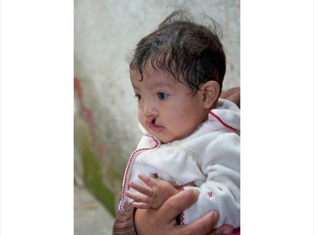Baby in a white outfit being held, looking down with a calm expression.