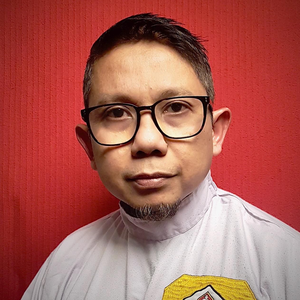 A man wearing glasses and a white shirt is standing in front of a red wall.