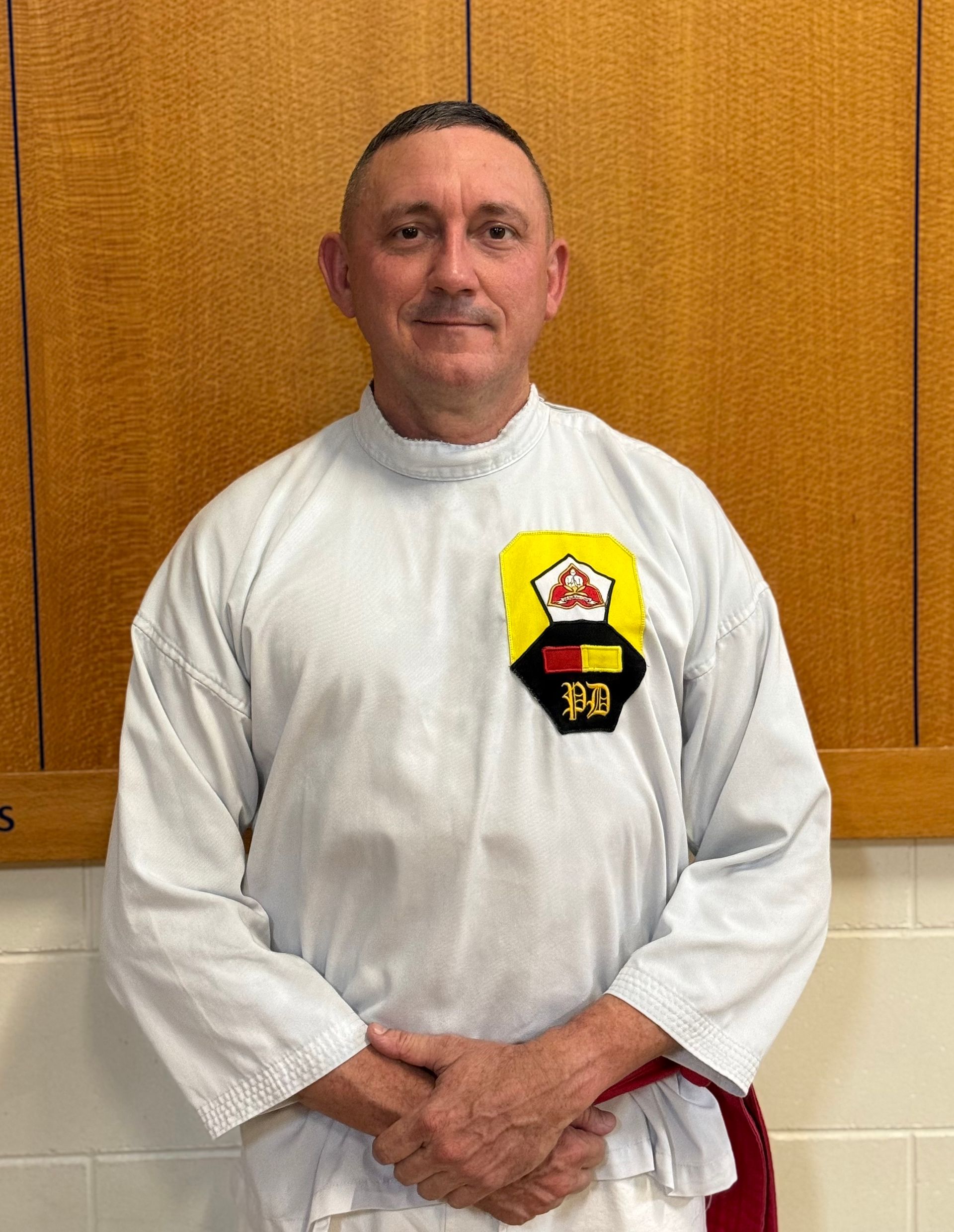 A man in a white karate uniform is standing in front of a wooden cabinet.