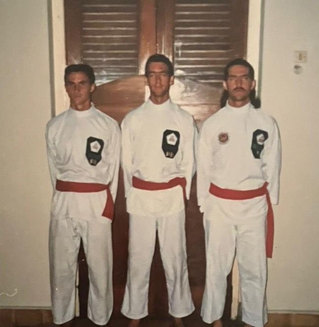 Three men in white karate uniforms stand in front of a door