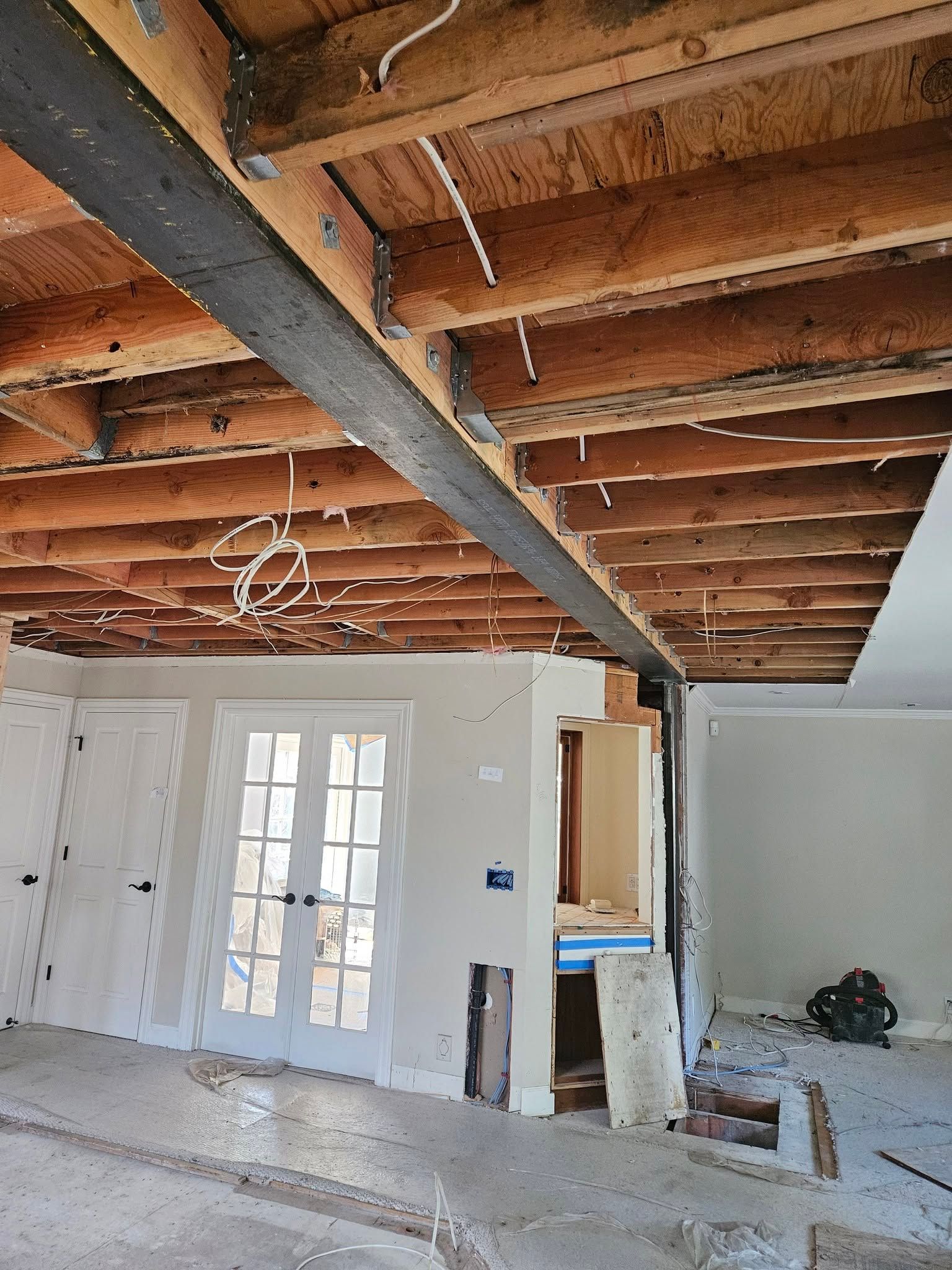 Exposed-beam room under renovation with white walls, French doors, and construction debris on the floor