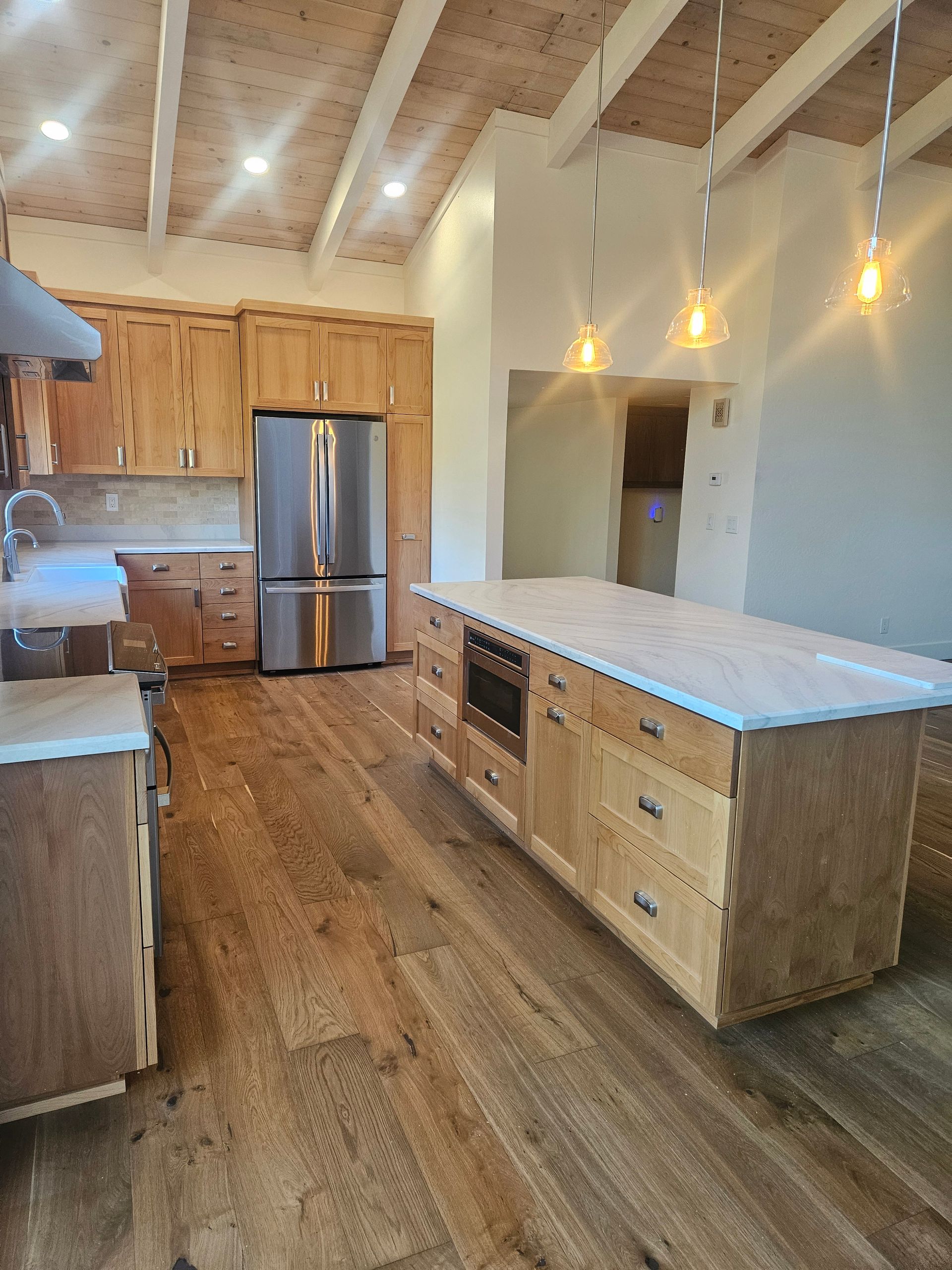 Modern kitchen with stainless fridge, wood floors, white island, and pendant lights under vaulted ceiling