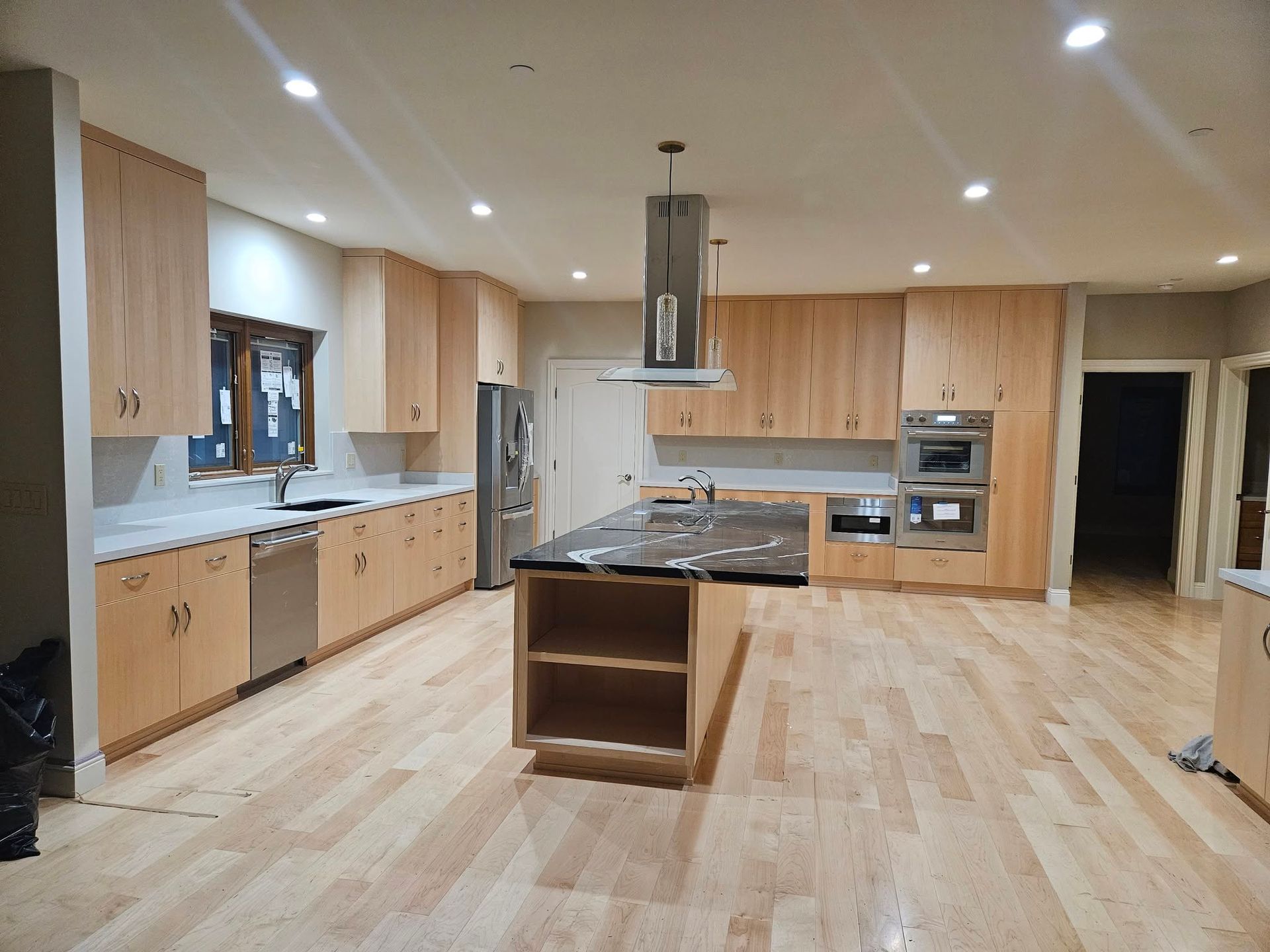 Spacious modern kitchen with light wood cabinets, island, and stainless steel appliances under recessed lights