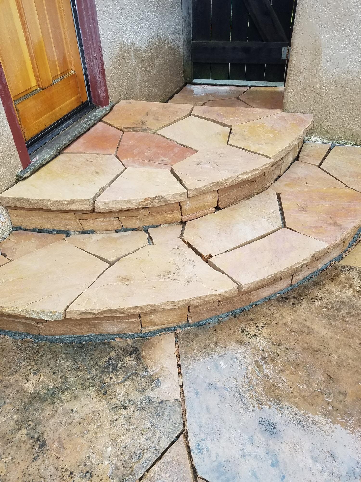 Stone front steps with curved edges leading to a doorway, set into a rough concrete walkway.
