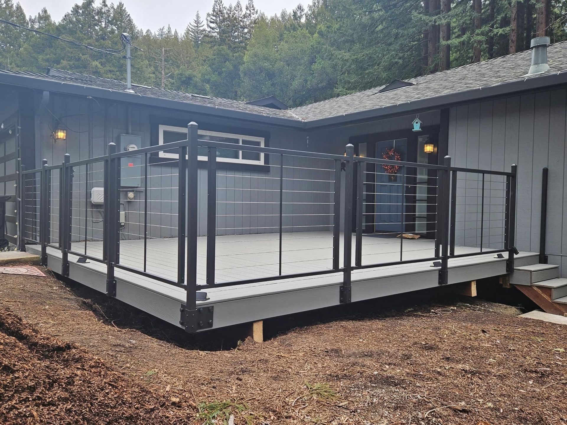 Modern cabin deck with black railings, gravel ground, and tall pine trees in the background