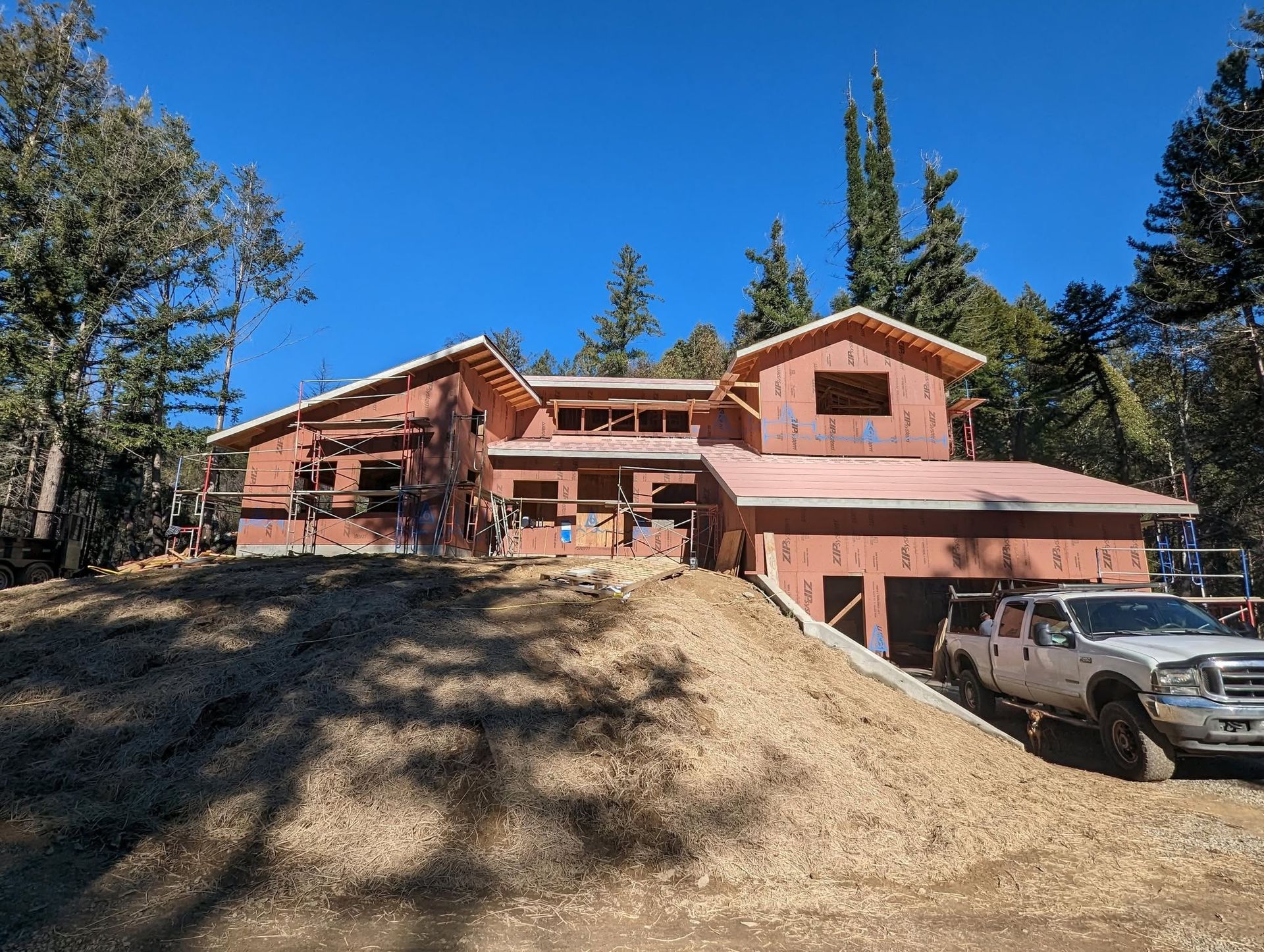 Rustic red house on a hillside with trees and parked cars under a bright blue sky