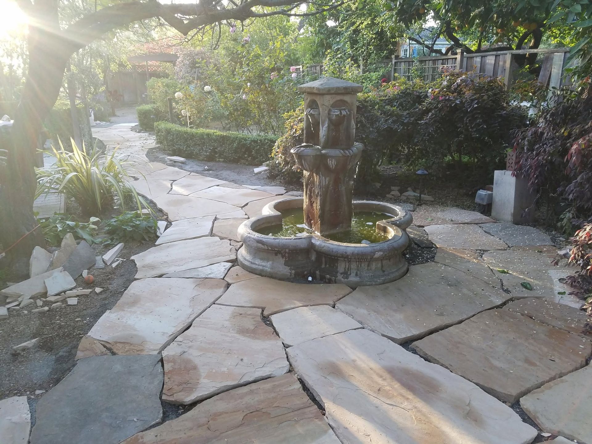 Sunlit stone patio with a small central fountain surrounded by greenery