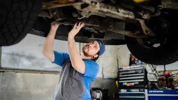 Mechanic in blue cap inspecting the underside of a lifted vehicle in a garage