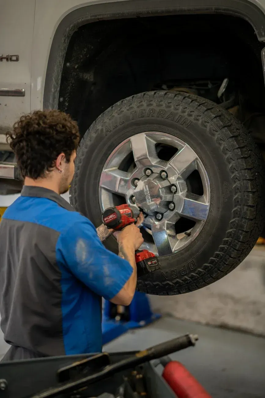 Mechanic using a red impact wrench to tighten lug nuts on a truck tire in a garage