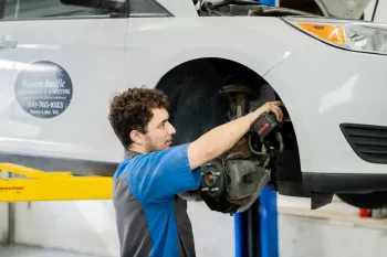 Mechanic repairing the front wheel of a silver car on a hydraulic lift