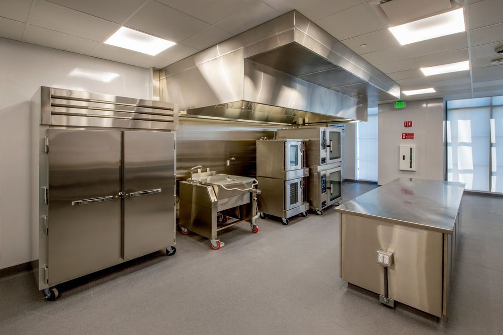 Modern commercial kitchen with stainless steel appliances and prep tables under bright ceiling lights
