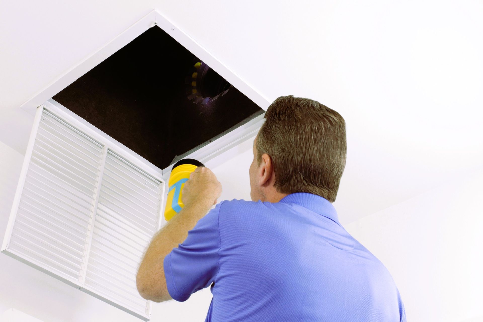 A man wearing a blue shirt cleaning air vent ducts