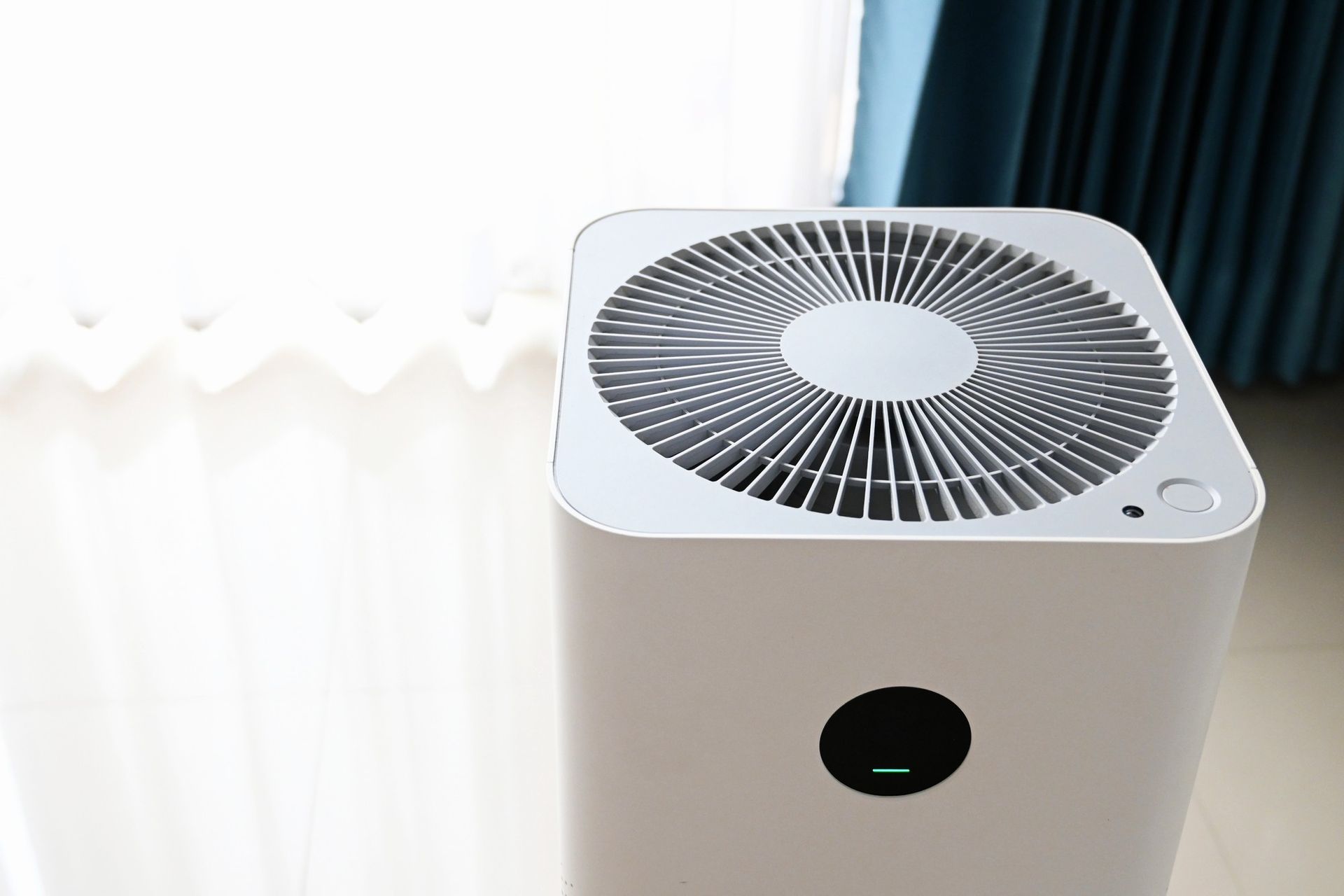 Air purifier in a bright room with a curtain in the background.