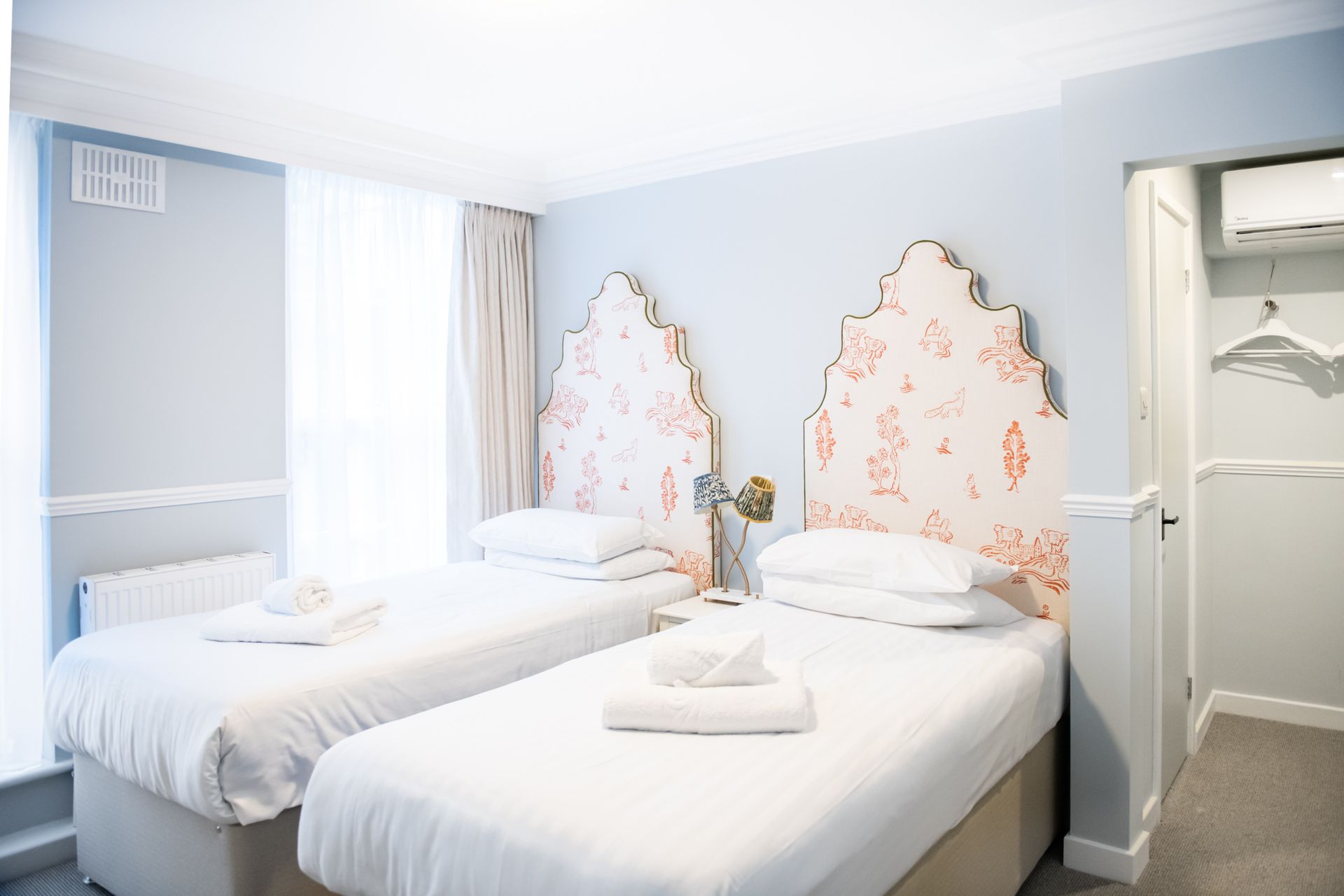 Twin hotel room with floral headboards, light blue walls, and a small doorway.