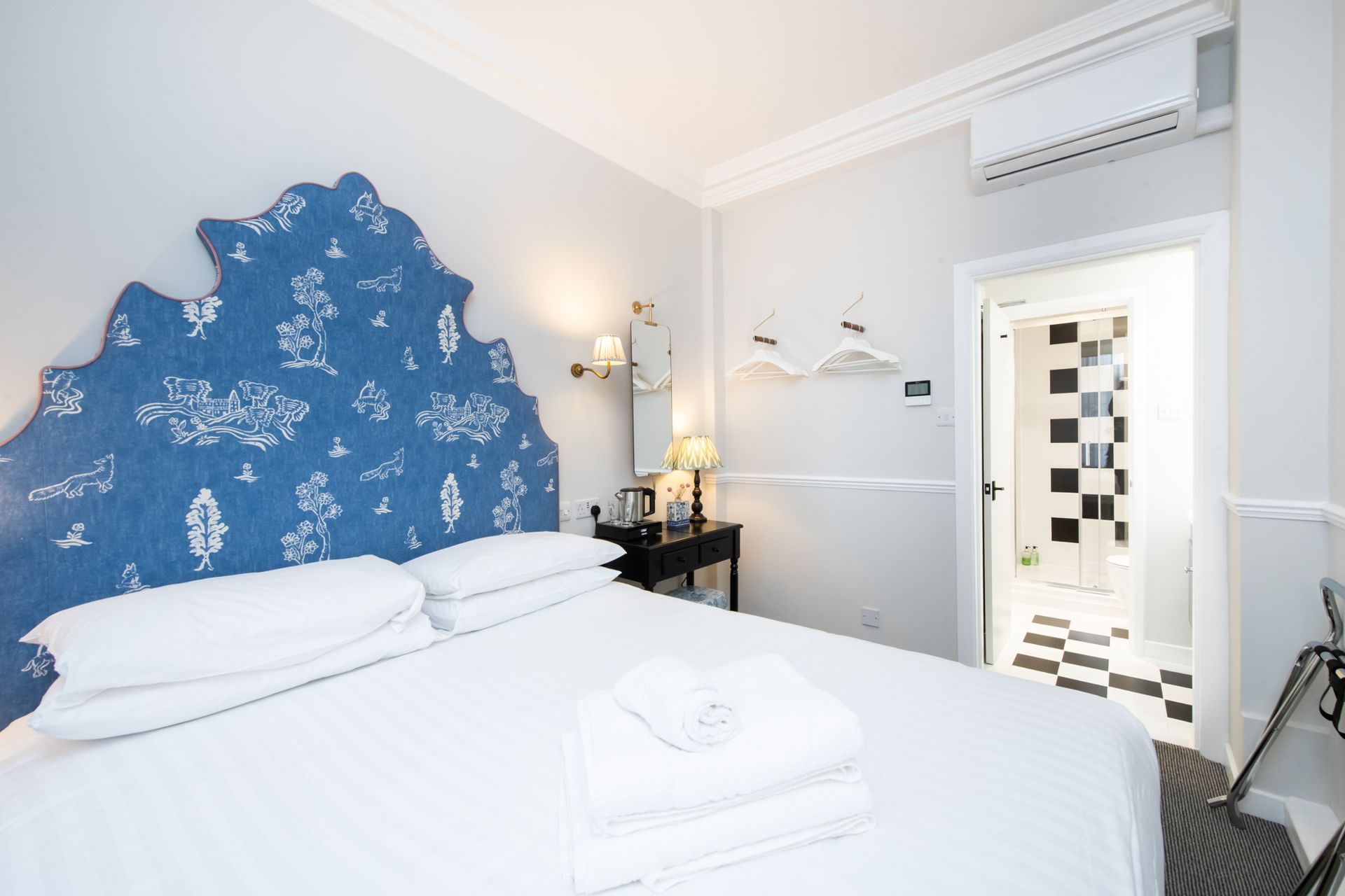 Bedroom with blue floral headboard, white bedding, black side table, and open bathroom door.