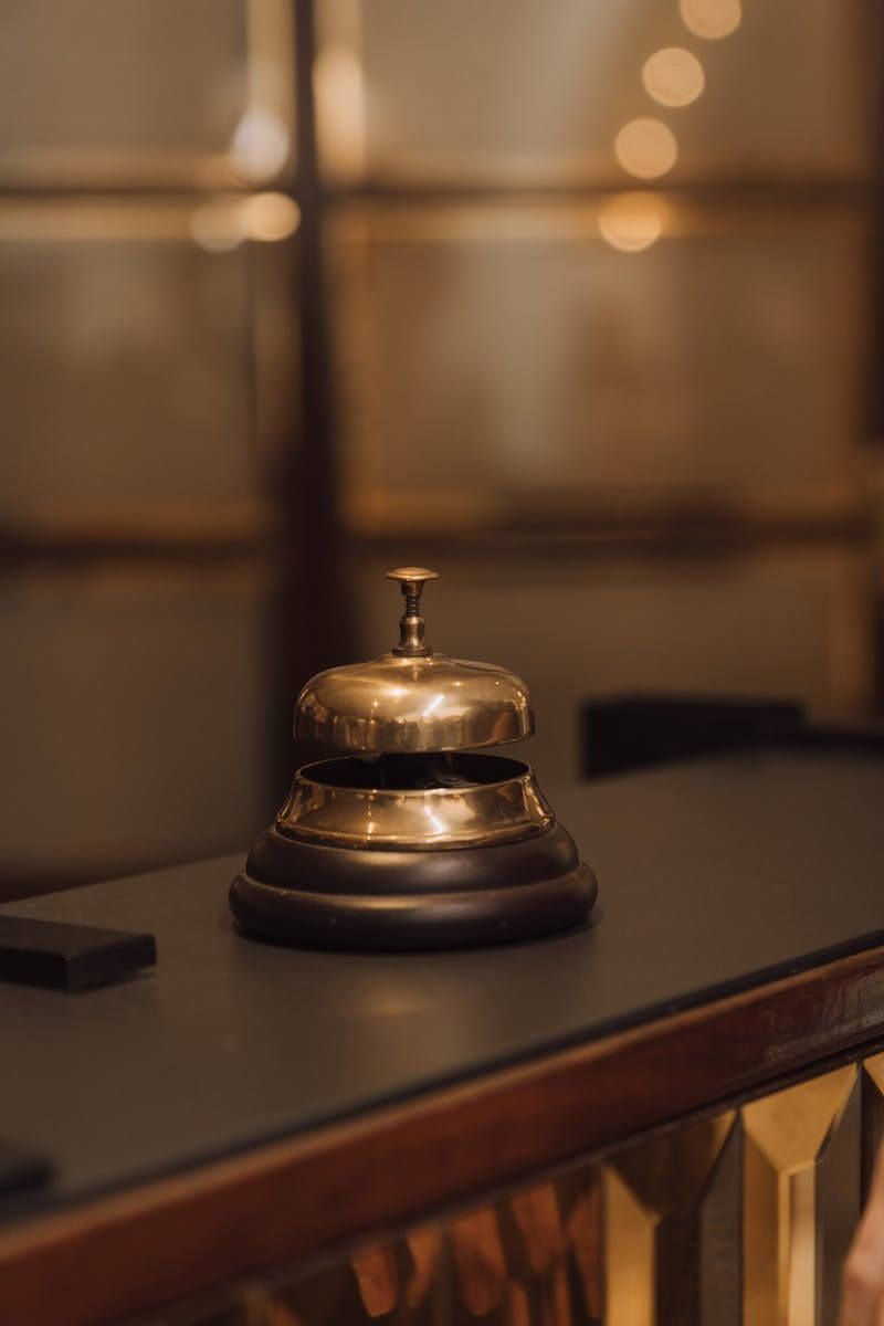 Brass hotel bell on a wooden base sits on a dark counter.