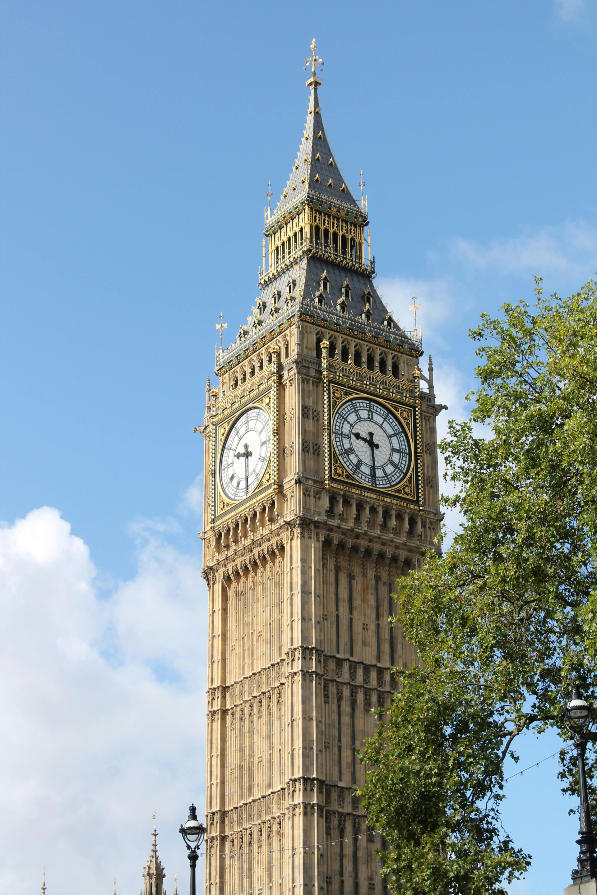 Clock tower of the Palace of Westminster, London, with gold accents and a clear blue sky.