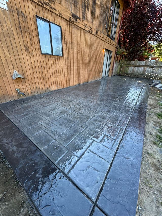 Wet concrete patio beside a wood building, with windows and a fence in the background.