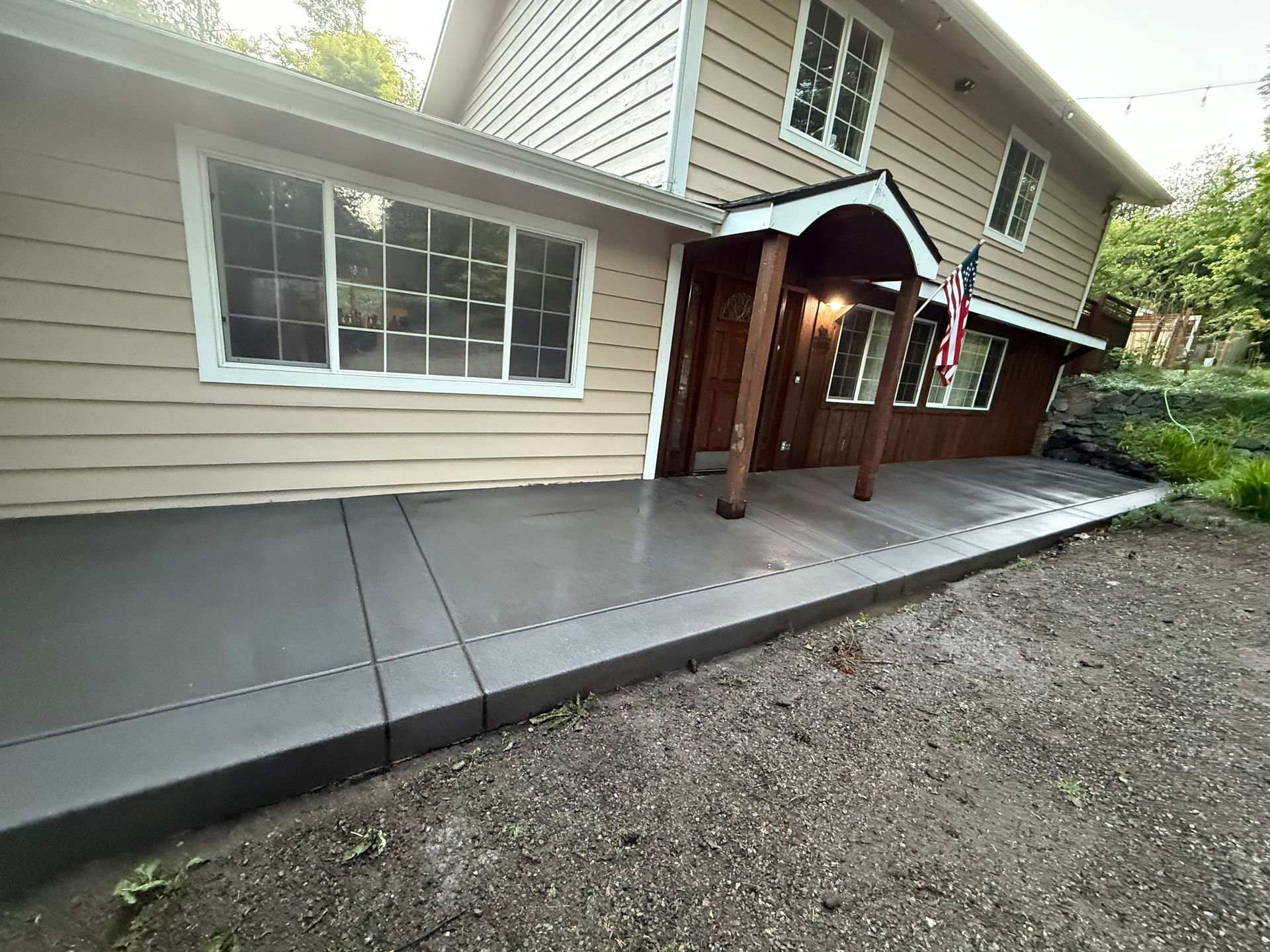Concrete side ramp along beige house exterior beside a gravel yard, leading to a covered porch.