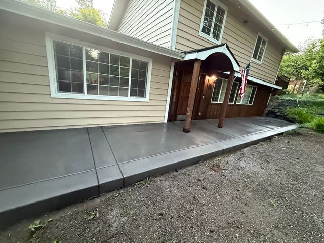 Concrete side ramp along beige house exterior beside a gravel yard, leading to a covered porch.