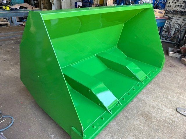 A Green Bucket is Sitting on the Ground in a Garage — Wingham Farm Machinery in Wingham, NSW