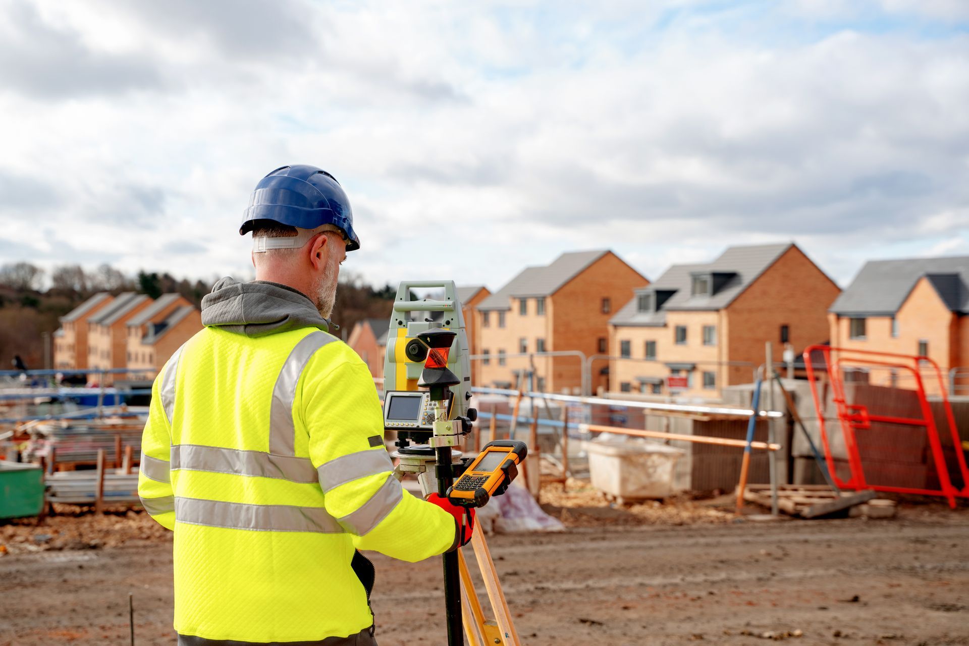 Surveyor using a total station near a residential construction site.