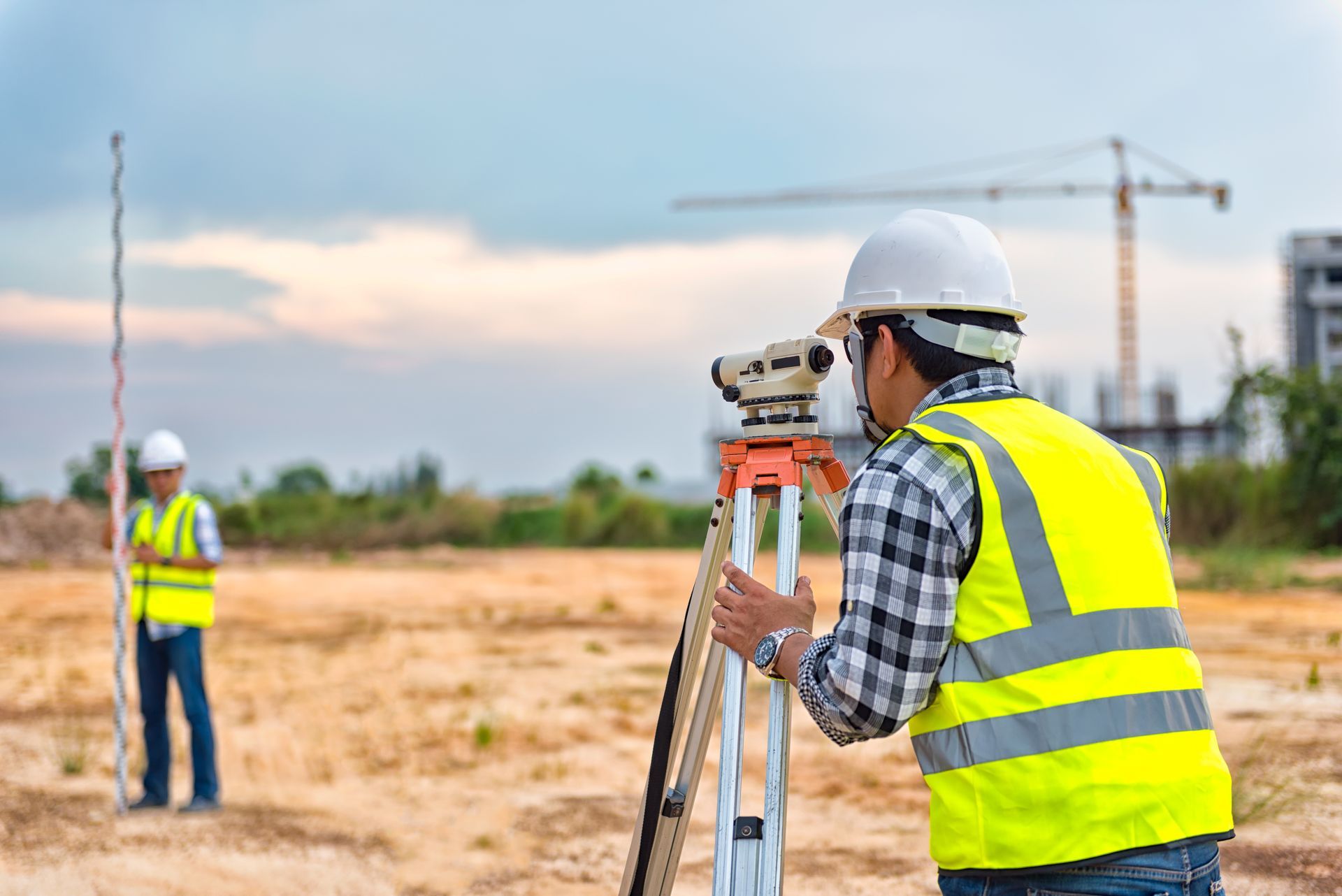 Surveyor using a theodolite on tripod, measuring land at construction site.