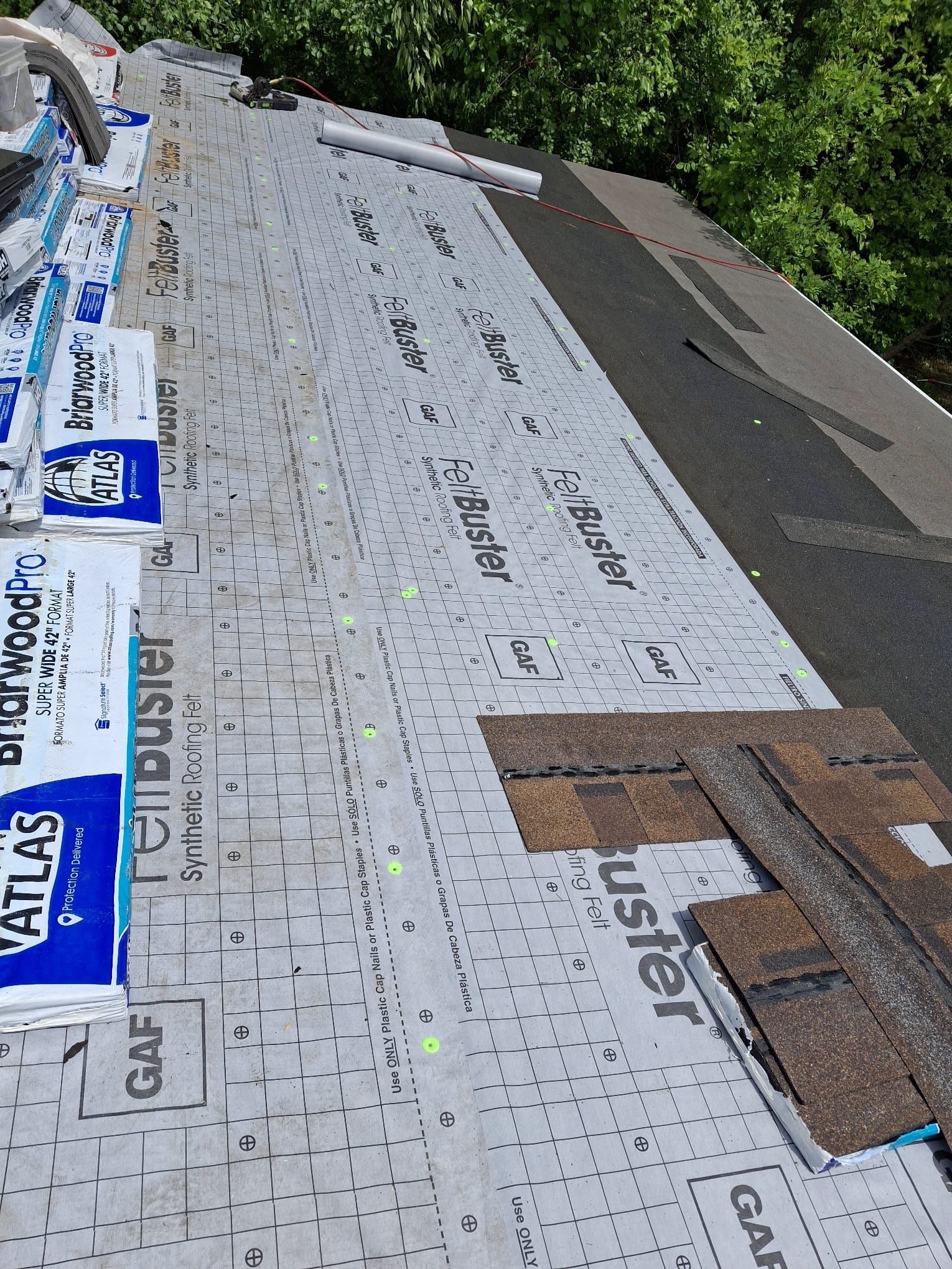 Roof under construction with white underlayment, roofing nails, and bundles of materials along the edge