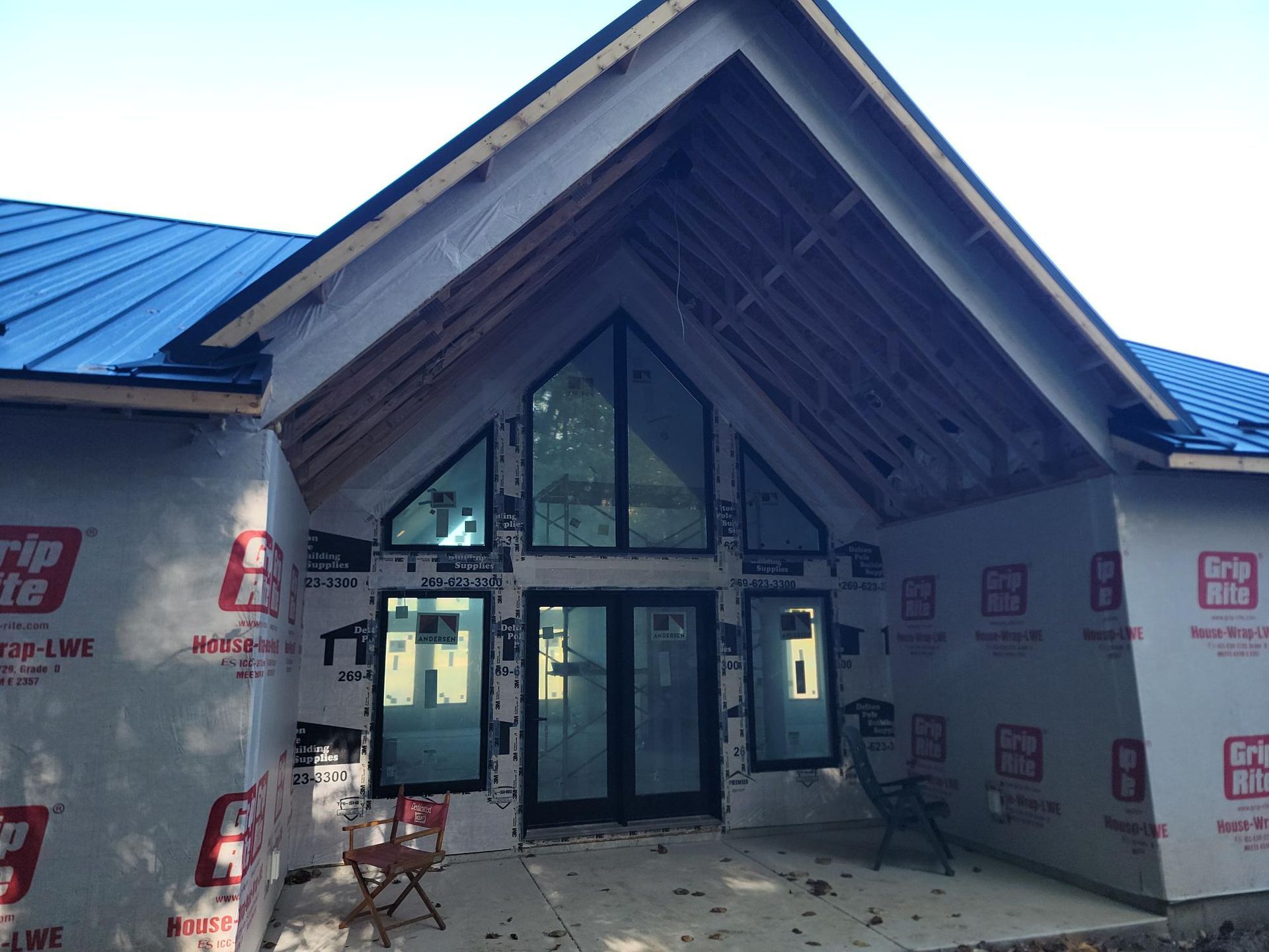 Front entrance of a house under construction with blue metal roofing and exposed wall sheathing.