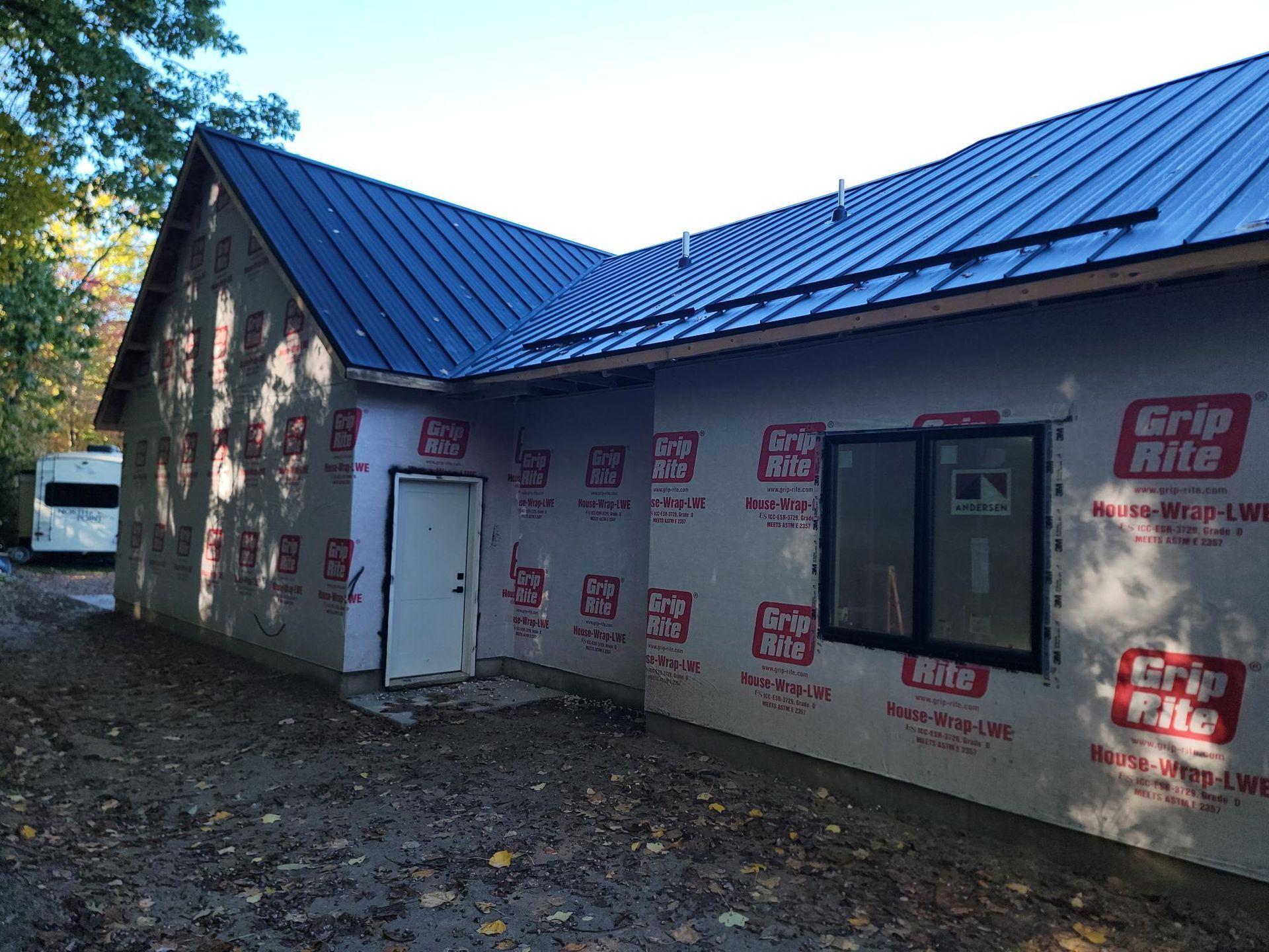 Partially finished house with blue metal roof and exposed wall insulation under construction