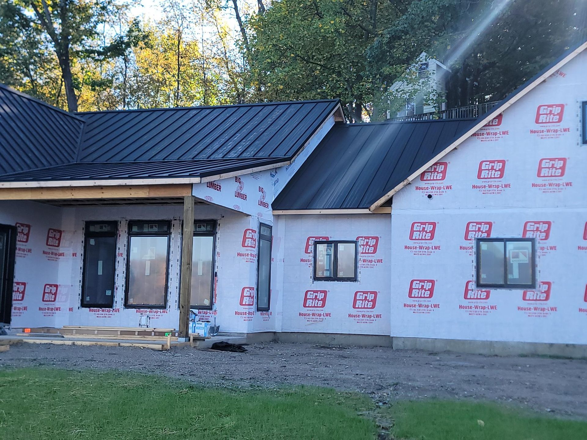 Partially built house with black metal roofs and wrapped exterior walls at a wooded site