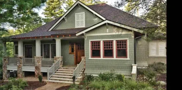 Gray bungalow house with green trim, front porch, and steps under trees