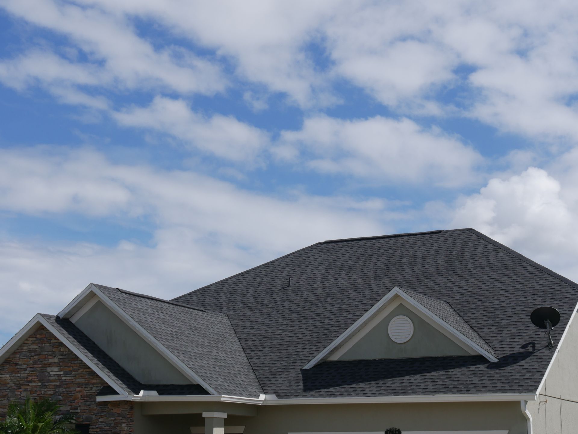 Suburban house rooftops with gray shingles beneath a partly cloudy blue sky