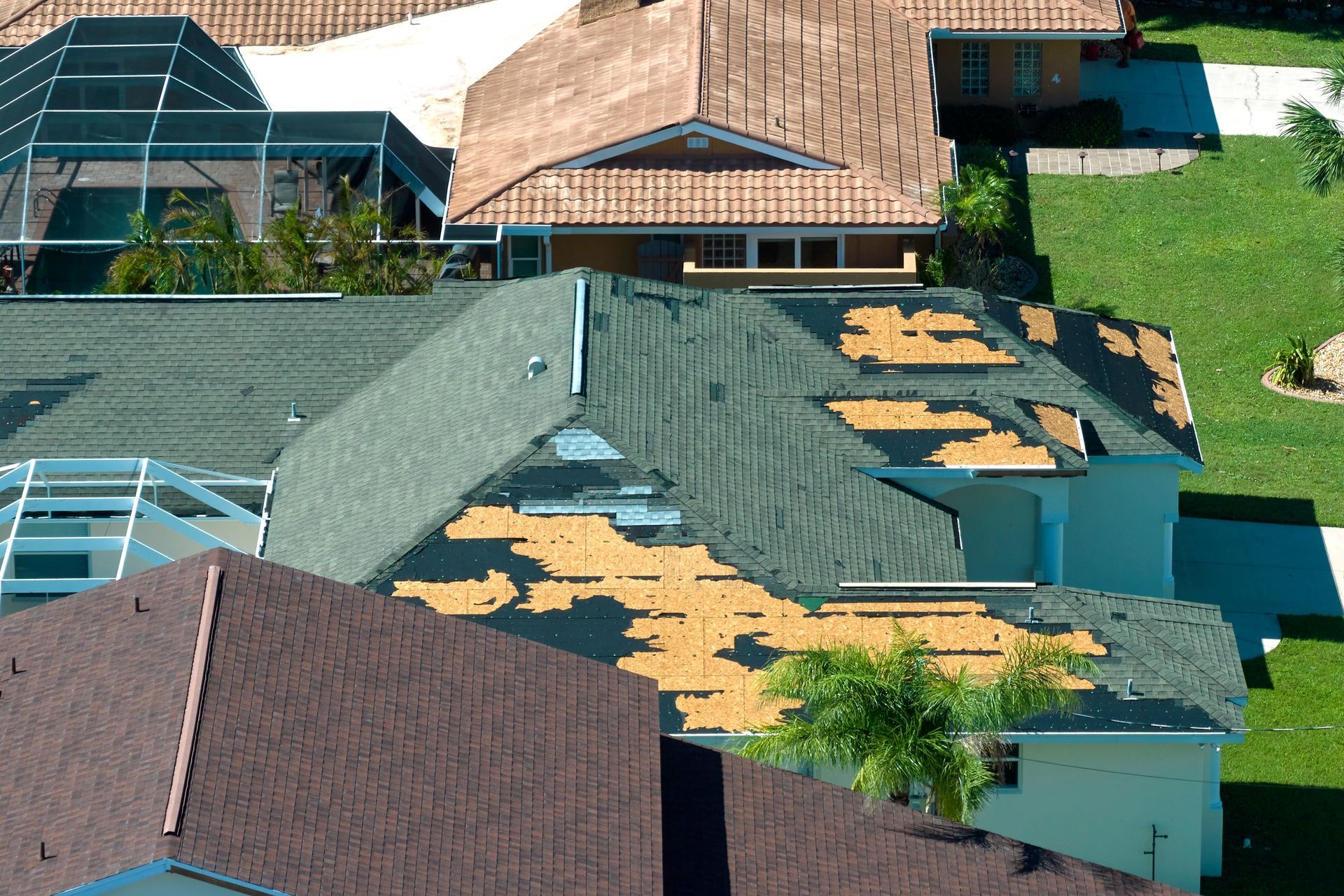 Rooftop view of houses with damaged green shingles and exposed wood patches after storm damage