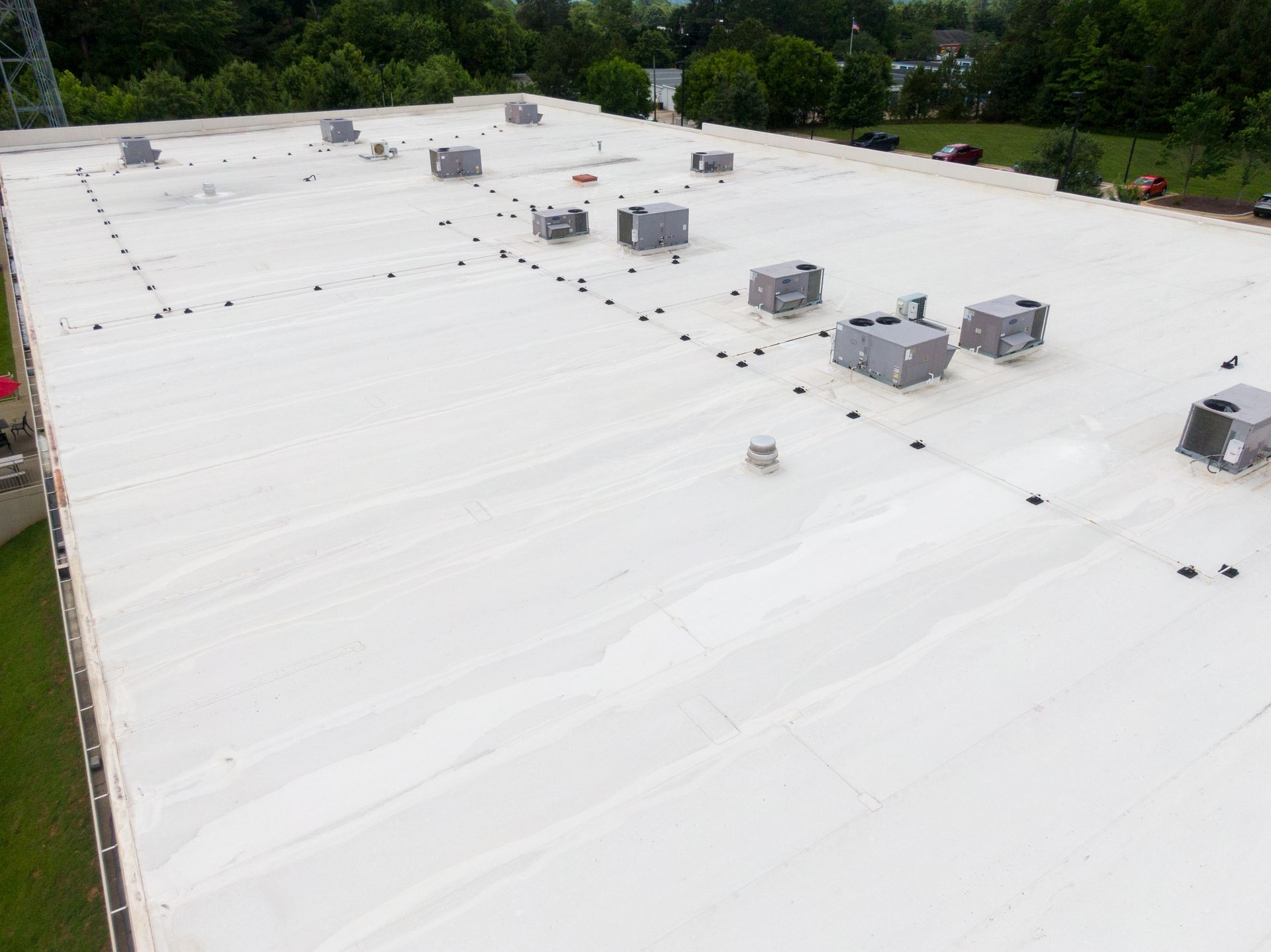 White commercial rooftop with several HVAC units and surrounding trees under clear daylight