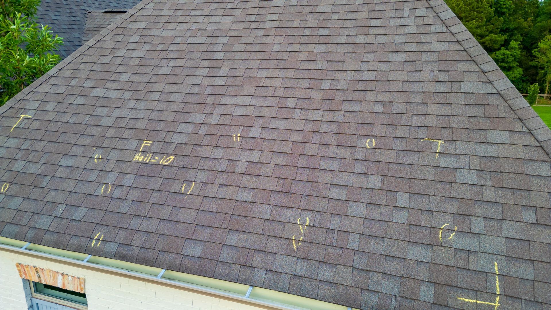 Gray shingle roof with several small patches of damage and a white house edge visible below