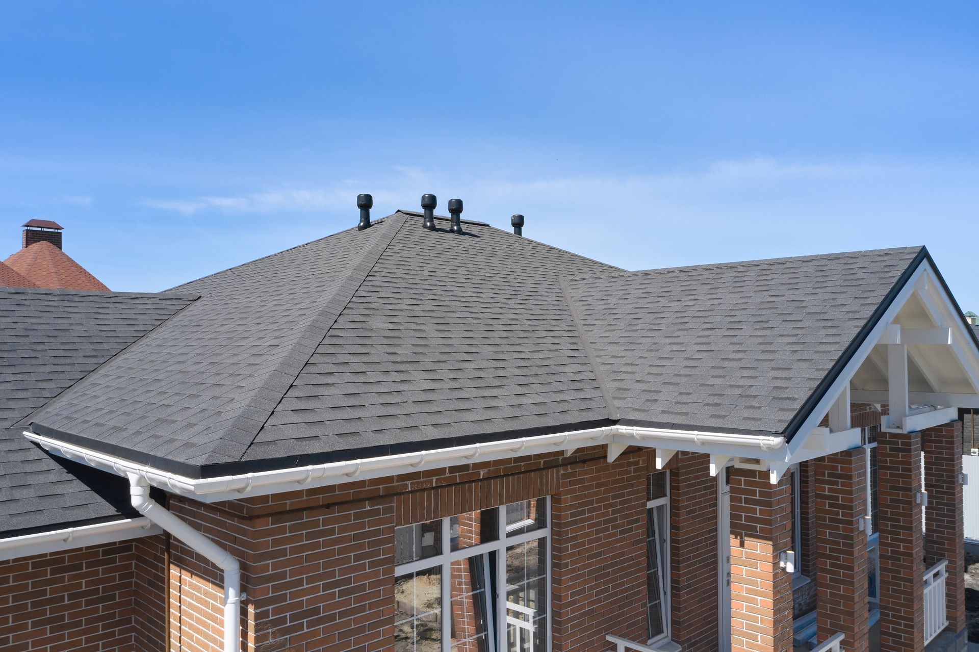 Brick house with a dark gray shingled roof under a blue sky