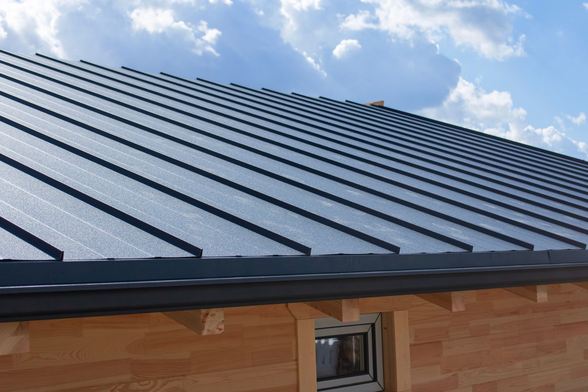 Dark metal roof on a wooden house under a blue, cloudy sky