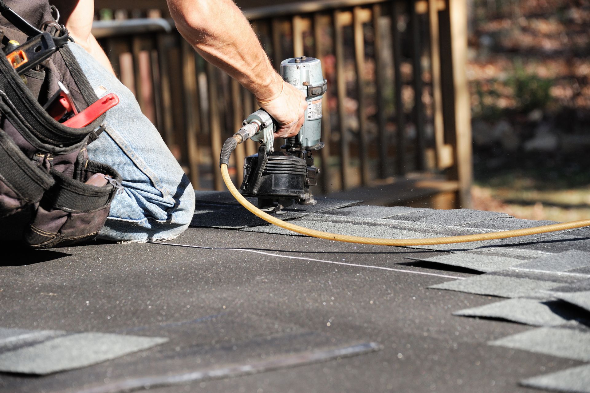 Worker using a power tool to cut roofing material on a rooftop, with scattered shingles nearby