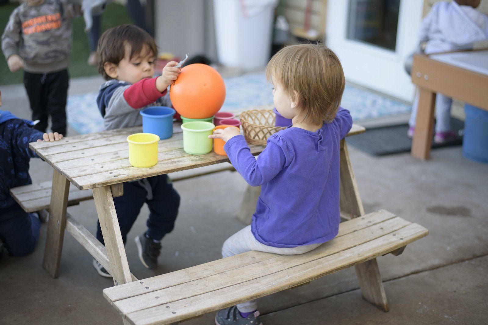 Two young children are sitting at a picnic table playing with toys.