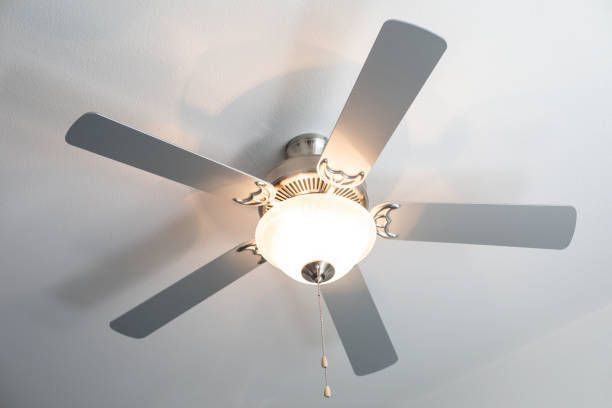 Five-blade white ceiling fan with light fixture and pull chain mounted on home interior ceiling.