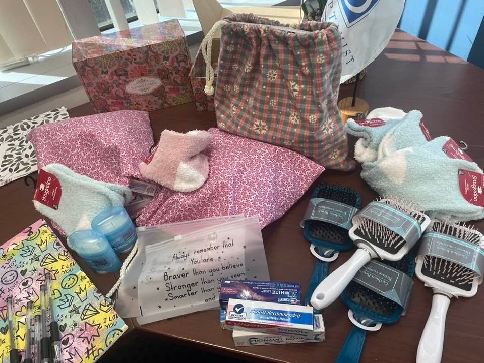 A collection of care package items including socks, hairbrushes, toiletries, and note cards spread across a table.