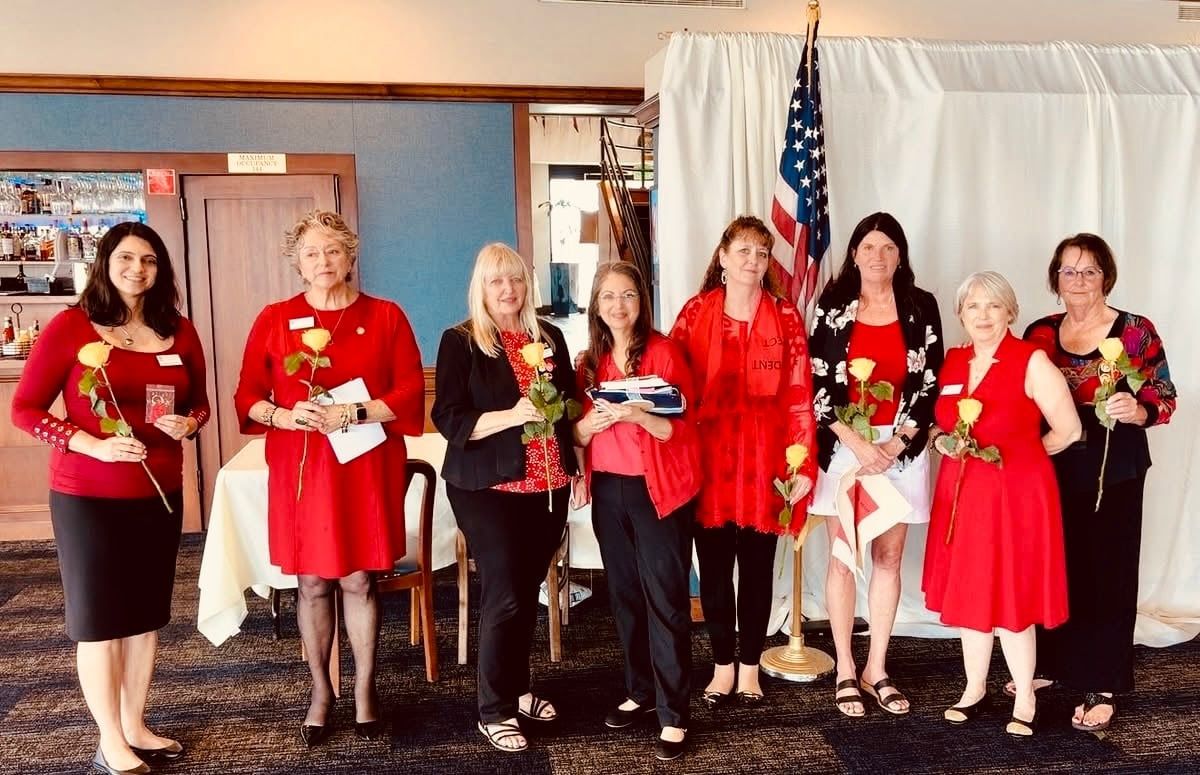 Seven people in red and black outfits standing on a stage holding flowers and certificates.