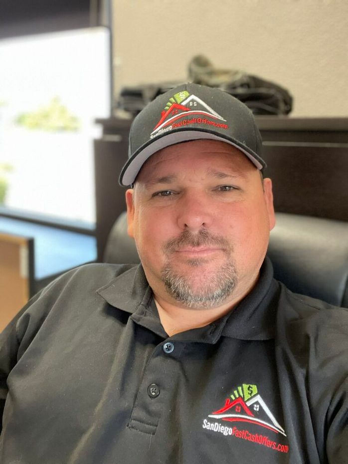 Man in a black cap and polo shirt seated at a desk in an office, looking at the camera