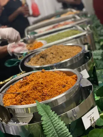 Buffet line with stainless-steel trays of orange and brown rice dishes, served indoors