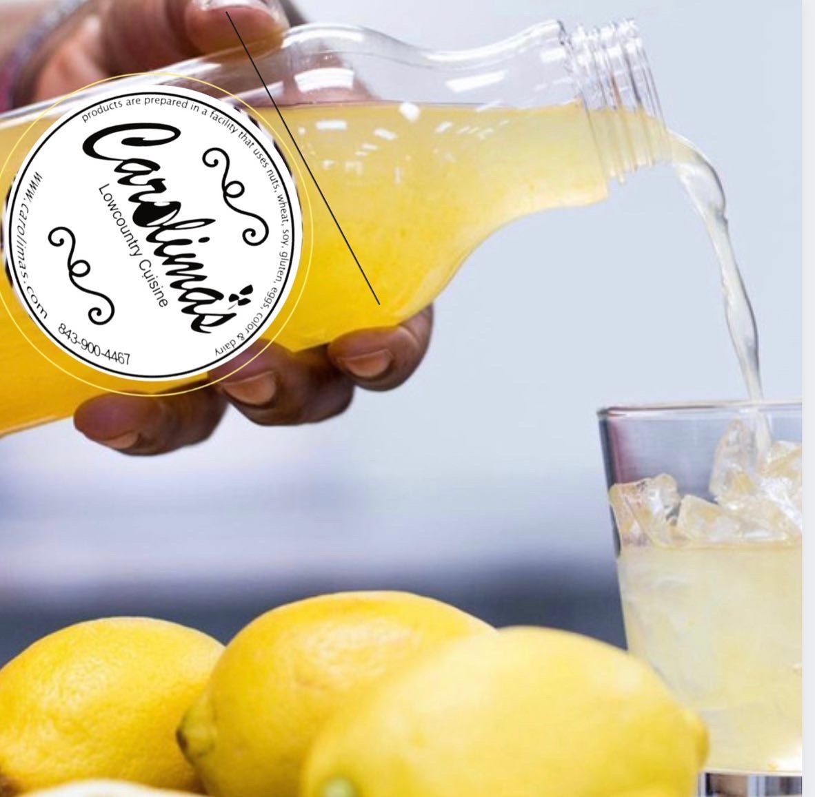 Hand pouring lemonade from a Carutina bottle into a glass beside lemons