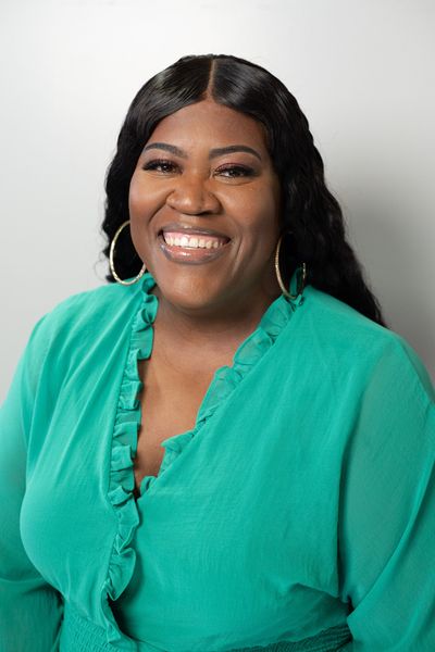 Smiling woman in a teal blouse against a light gray background