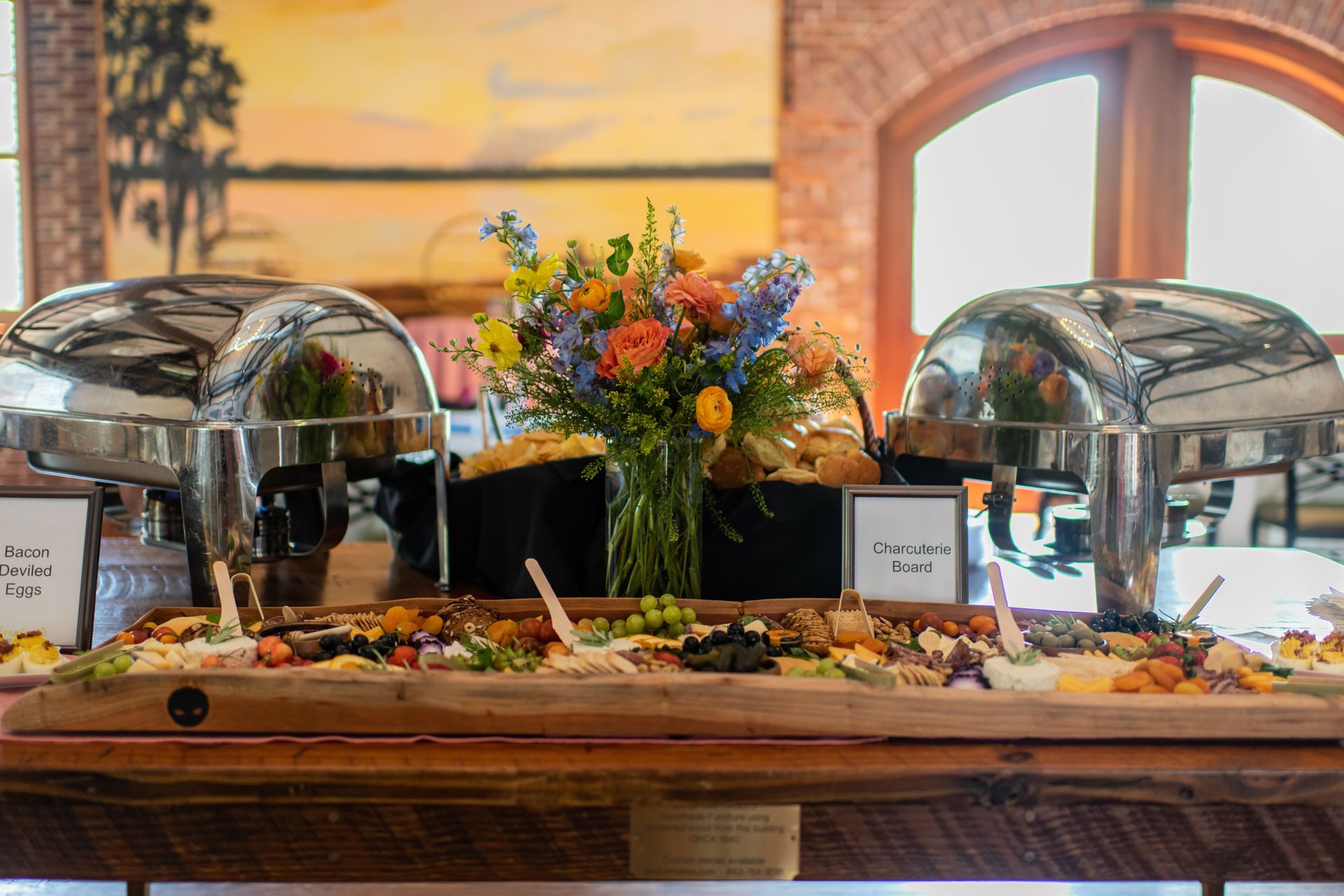 Buffet table with two silver chafing dishes, assorted dishes, and a colorful floral centerpiece in a warm dining room